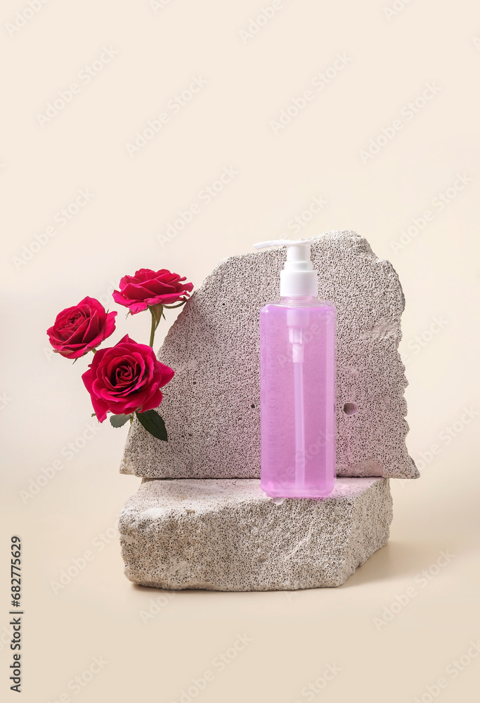 Pump bottle for cosmetics on the podium made of stone and roses on a beige background Pump bottle for cosmetics on the podium made of stone and roses on a beige background