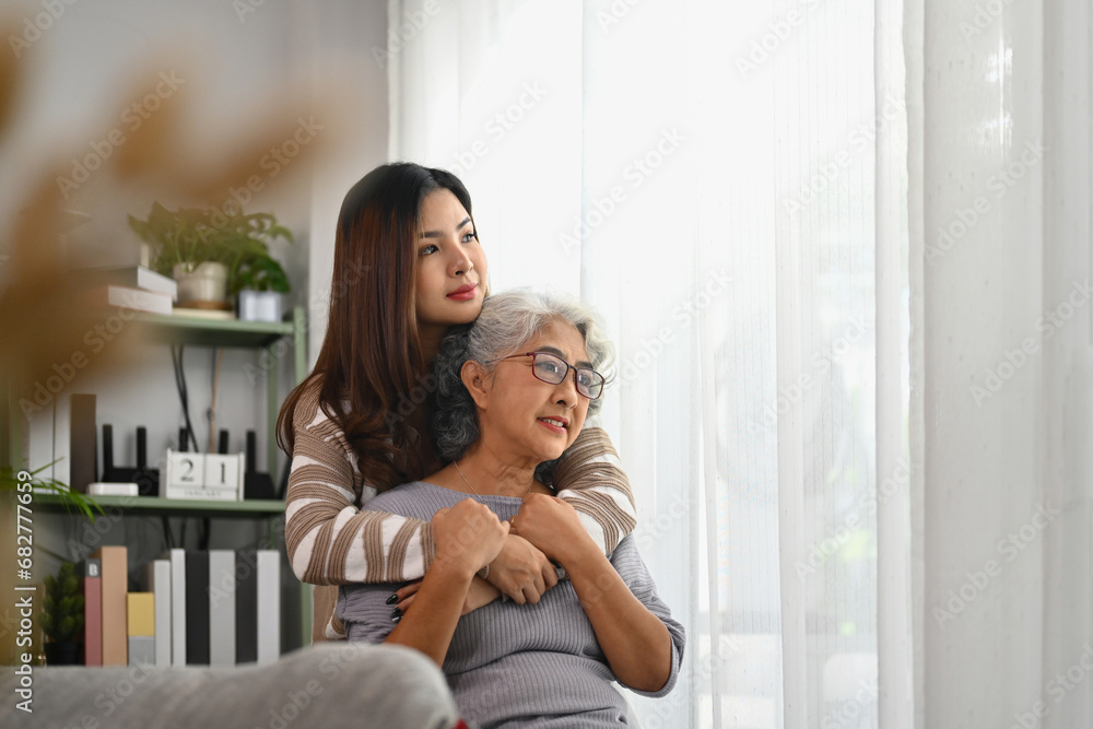 Beautiful moment of loving grown up daughter hugging mature mother from back Beautiful moment of loving grown up daughter hugging mature mother from back