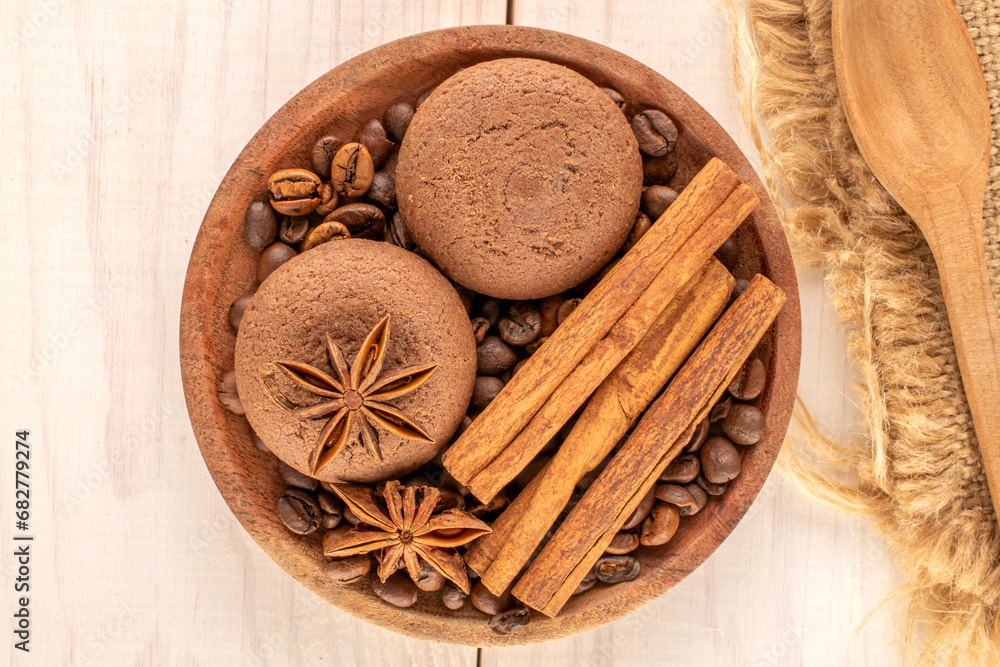 Chocolate cookies, cinnamon, star anise, coffee beans on a ceramic saucer with a cup on a wooden table, macro, top view. Chocolate cookies, cinnamon, star anise, coffee beans on a ceramic saucer with a cup on a wooden table, macro, top view.