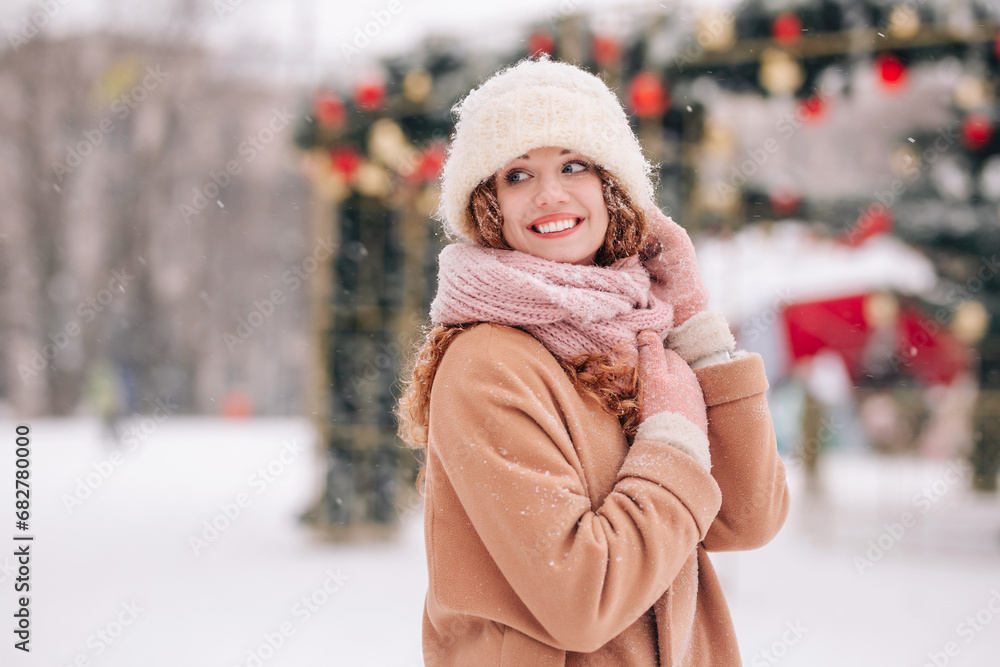 Charming curly woman posing against the background of a New Year tree in a city park. A girl in winter clothes walks through a snowy city.