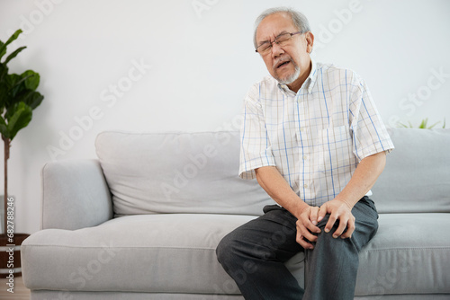 senior man suffering from knee ache on sofa