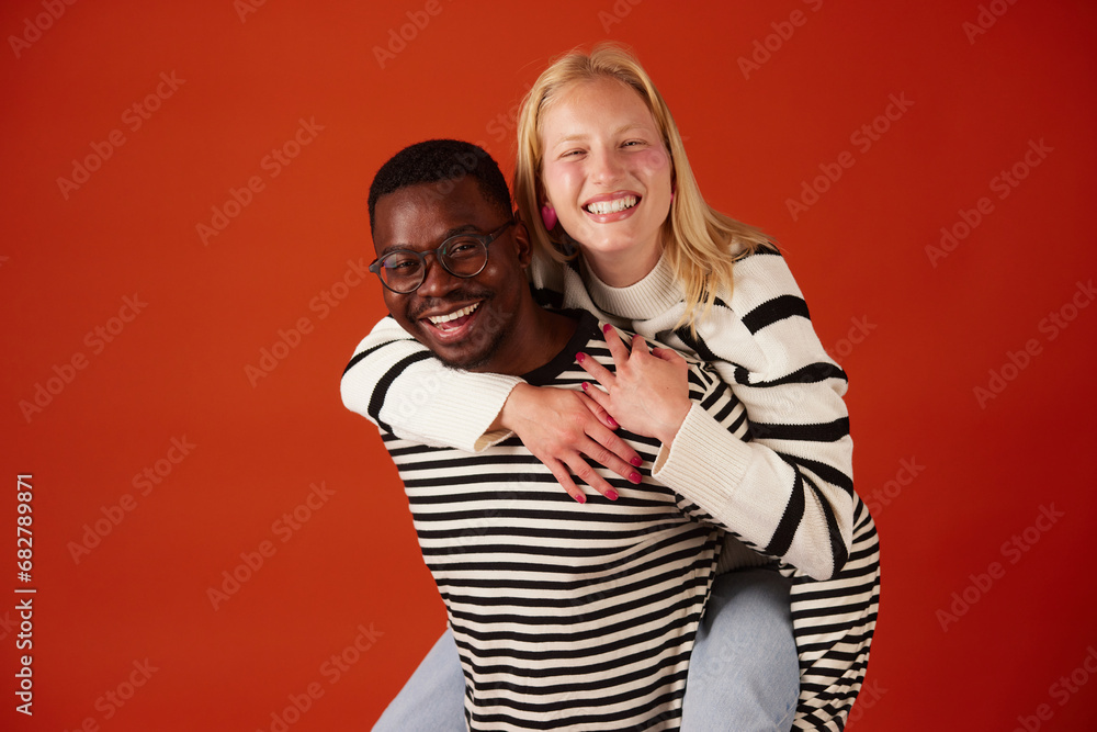 Obraz premium Joyful multiracial couple having fun together piggybacking over orange background