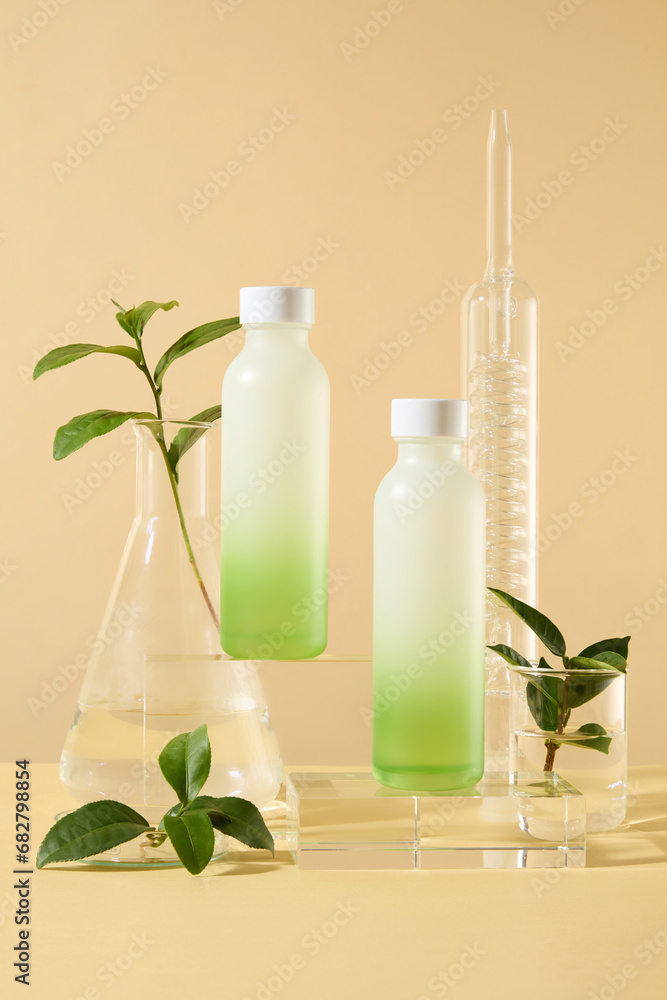 Set of cosmetic bottles on glass podiums with green tea leaves and lab glassware on beige background. Product and promotion concept for advertising cosmetic of green tea extract. Front view Set of cosmetic bottles on glass podiums with green tea leaves and lab glassware on beige background. Product and promotion concept for advertising cosmetic of green tea extract. Front view
