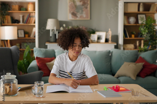 Bored African American teenager doing homework without interest at home photo
