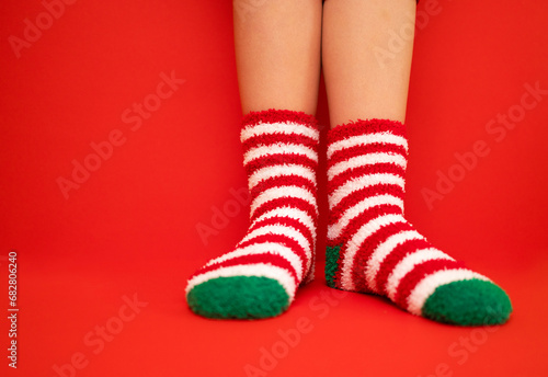 Female feet in fluffy New Year or Christmas warm socks. The colors of the socks are red and white stripes and green heels and tips. Girls legs on a red bright background.