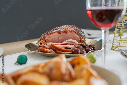 Medium close-up of christmas composition with baked Christmas ham or gammon on dark background. Traditional food concept. Plate with delicious ham served on wooden table. Christmas dinner.