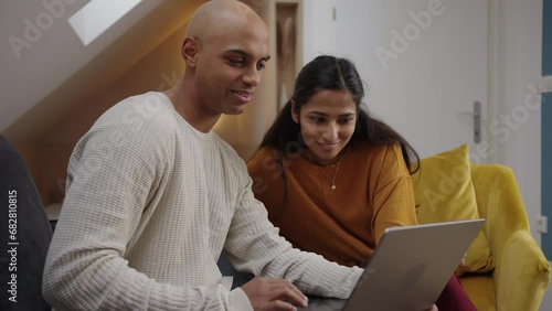 Two adults looking at a laptop and having relaxed conversation with someone over video meeting