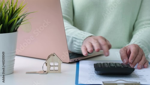 Woman calculating mortgage cost on calculator and entering data into laptop. Expenses on refinancing of home loan. Real estate investment concept photo