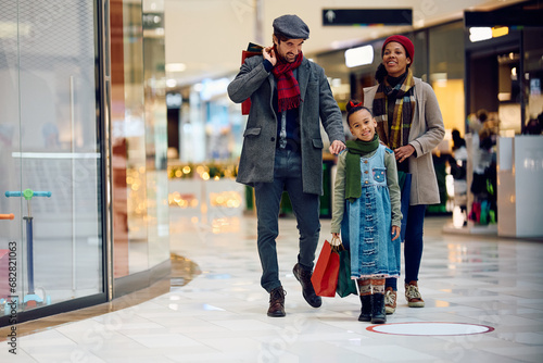 Happy black girl enjoys in shopping with parents at mall during winter holidays.