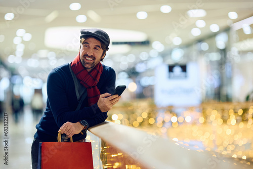 Happy man texting on cell phone while shopping at mall during winter holidays. photo