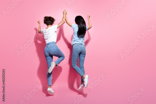 Full body size photo of active jumping two best friends hands together raise up trampoline rear back view isolated on pink color background