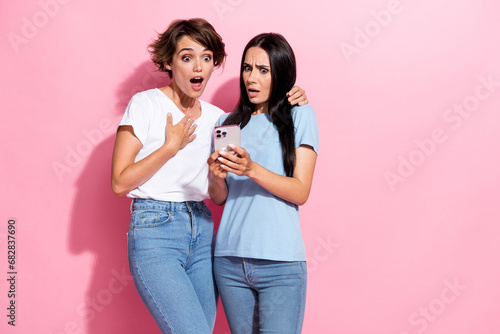 Photo portrait of two funny stressed confused girls shocked omg message smartphone ex boyfriend isolated on pastel pink color background photo