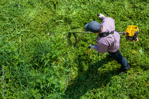 lawnmower man with a weed wacker or a string trimmer trimming grass at sunny day photo