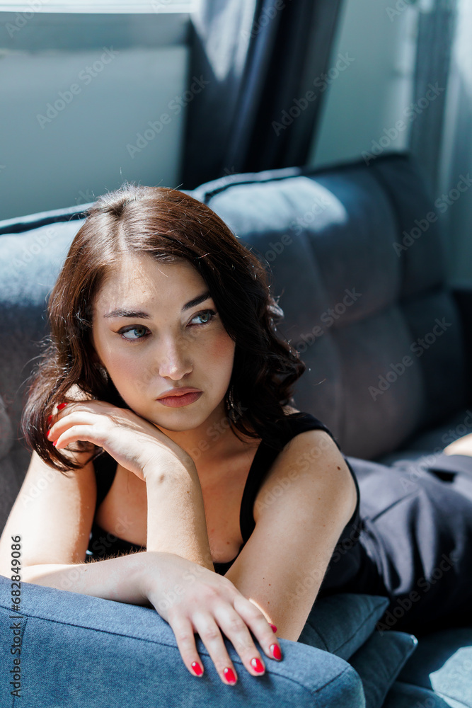 Young beautiful brunette girl in a black dress sitting on the sofa Young beautiful brunette girl in a black dress sitting on the sofa