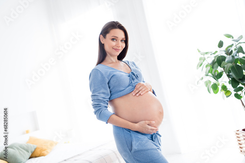 Photo of charming lovely tender gentle pregnant girl touching tummy waiting meet firstborn baby white light indoors photo