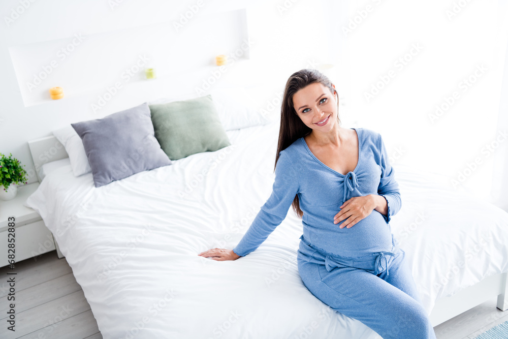 Photo of positive cute lovely mommy sitting on soft sofa cozy light room enjoying weekend relax rest touching belly Photo of positive cute lovely mommy sitting on soft sofa cozy light room enjoying weekend relax rest touching belly