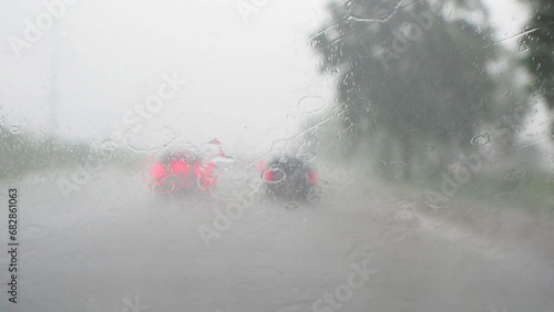 View through running car windshield during heavy rain. Wiper is cleaning the windshield glass. Traffic on highway during heavy rain in rainy season.