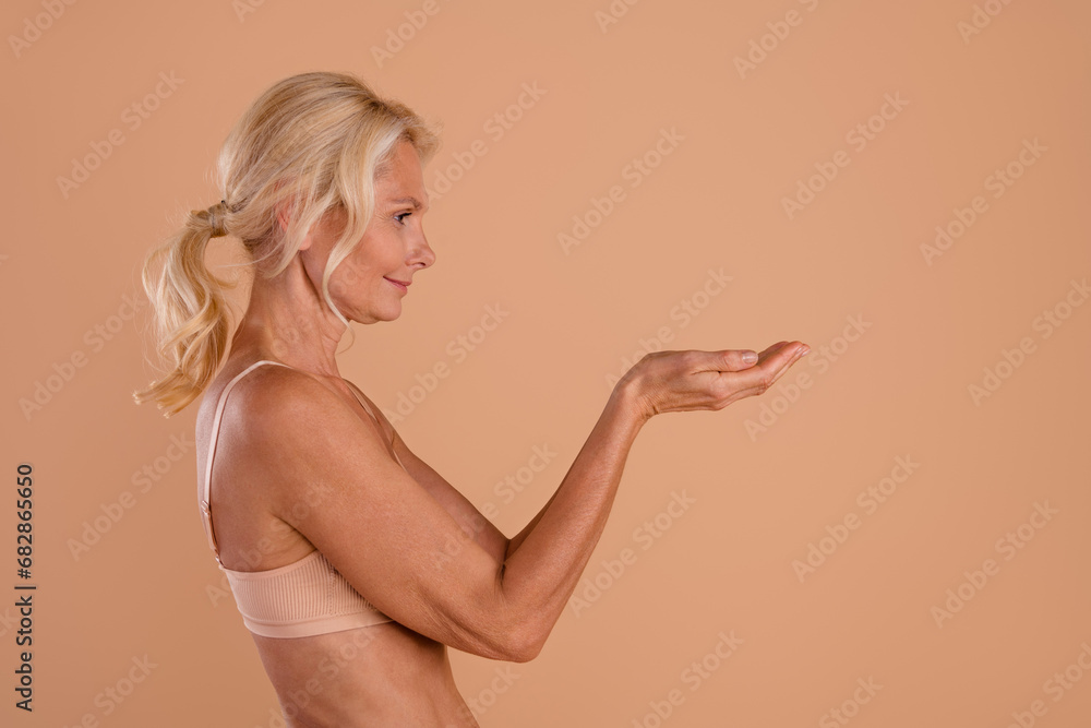 Photo of happy adorable middle age woman wear bikini showing arms looking empty space isolated beige color background