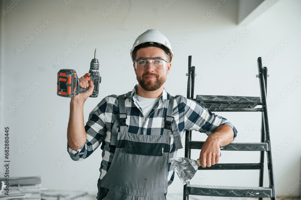 With drill. Repairman in uniform is in the unfinished building With drill. Repairman in uniform is in the unfinished building