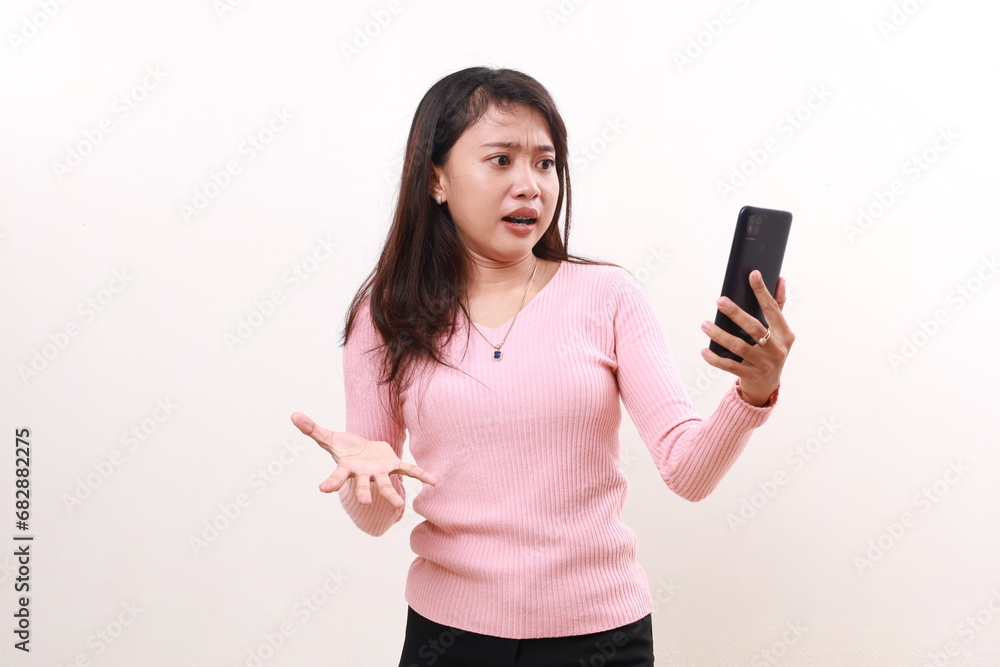 Unhappy angry young asian girl standing while holding a cell phone. Isolated on white background Unhappy angry young asian girl standing while holding a cell phone. Isolated on white background