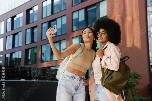 Two smiling female friends students taking selfies while standing in university campus © Drobot Dean