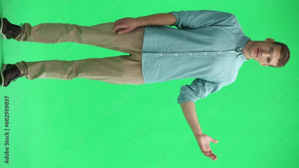 A young man on a green background in full growth shows his hand to the side A young man on a green background in full growth shows his hand to the side