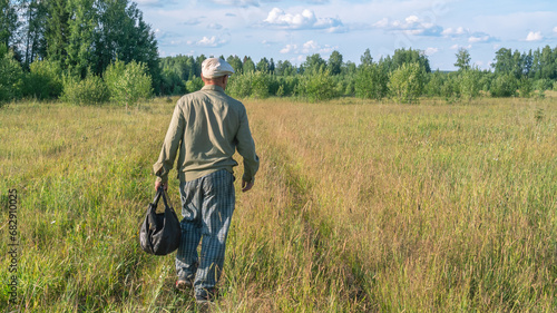 A road through a grassy field in the countryside. Nature in the village. Summer landscape in the village. An elderly man walks across the field. Vacation in the village.