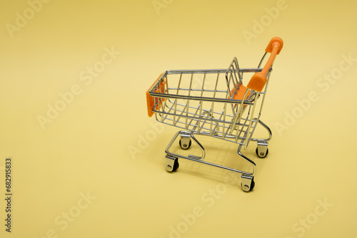 Small cart on a yellow background. Small supermarket grocery push cart for shopping. Shopaholic. Buyer. Shopping concept. Close-up. Isolated shopping trolley on a yellow background. Copy space.