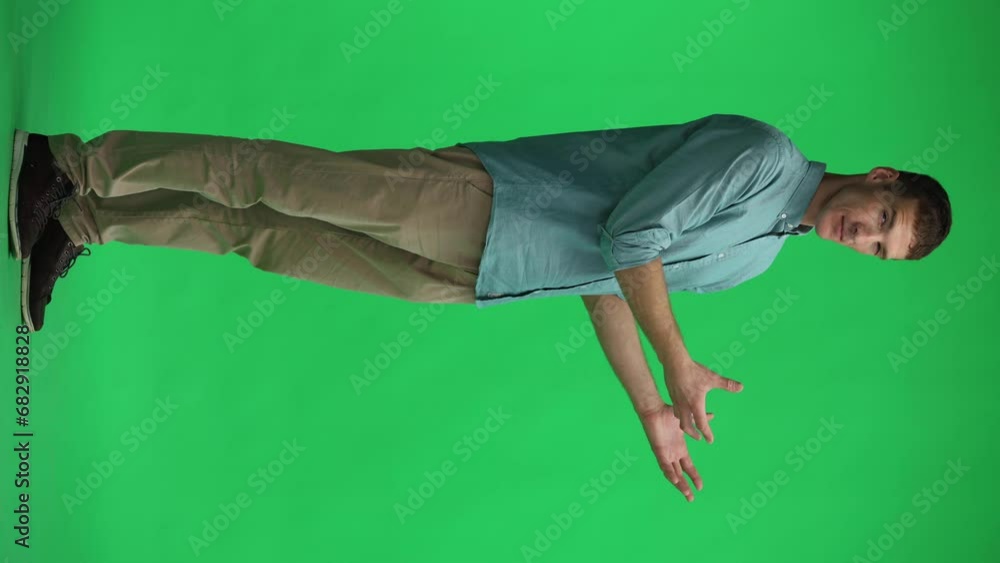 A young man on a green background in full growth shows his hand to the side A young man on a green background in full growth shows his hand to the side