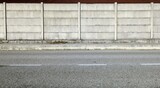 Grunge concrete precast compound wall at the road side with cement sidewalk and road in front. Background for copy space