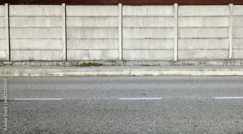 Grunge concrete precast compound wall at the road side with cement sidewalk and road in front. Background for copy space photo
