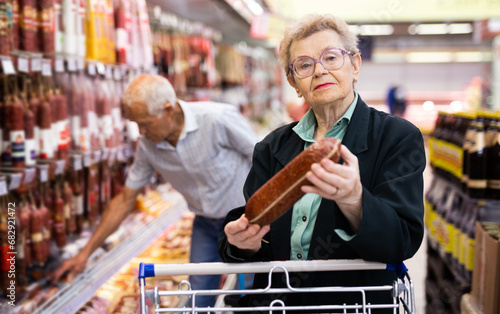 Mature woman with glasses picks out salami in the meat section of the supermarket