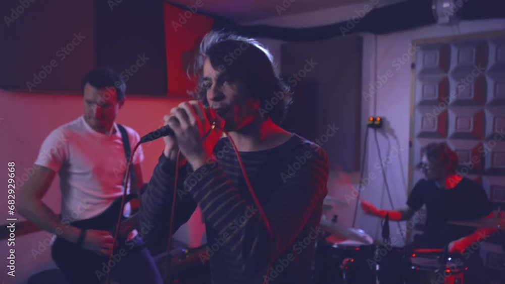 The singer sings the song into the microphone to the accompaniment of guitar and drums. Rehearsal of an amateur musical group in a garage equipped with a band room. The singer sings the song into the microphone to the accompaniment of guitar and drums. Rehearsal of an amateur musical group in a garage equipped with a band room.