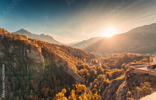Sunset shines over Briancon town with autumn forest and waterfall in Hautes Alpes, France