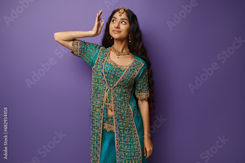 attractive young indian woman in traditional blue sari with accessories posing on purple backdrop
