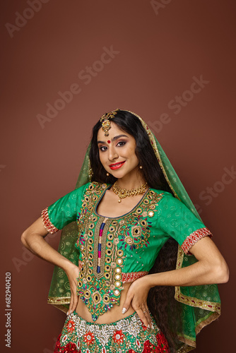 vertical shot of young indian woman in national clothes with arms akimbo smiling happily at camera