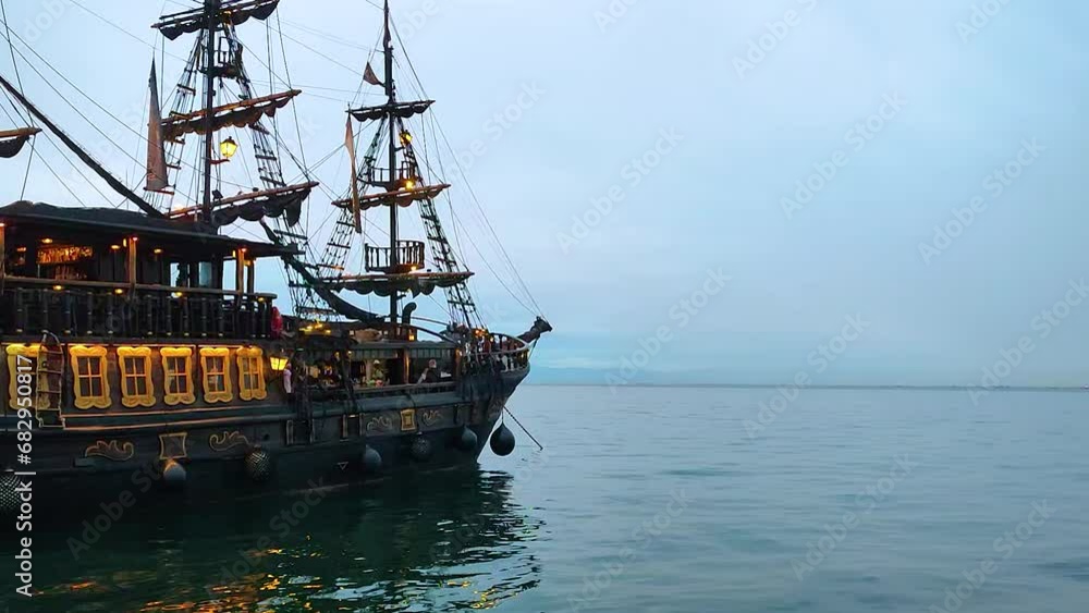 Old dark pirate ship with masts and weathered sails, sailing the sea with waves and the sky with clouds. Scene for an epic adventure and treasure story. Old dark pirate ship with masts and weathered sails, sailing the sea with waves and the sky with clouds. Scene for an epic adventure and treasure story.