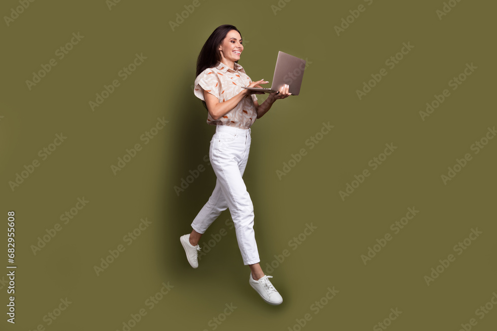 Full body size photo of funky mature startup developer woman jumping running with wireless computer isolated on khaki color background Full body size photo of funky mature startup developer woman jumping running with wireless computer isolated on khaki color background