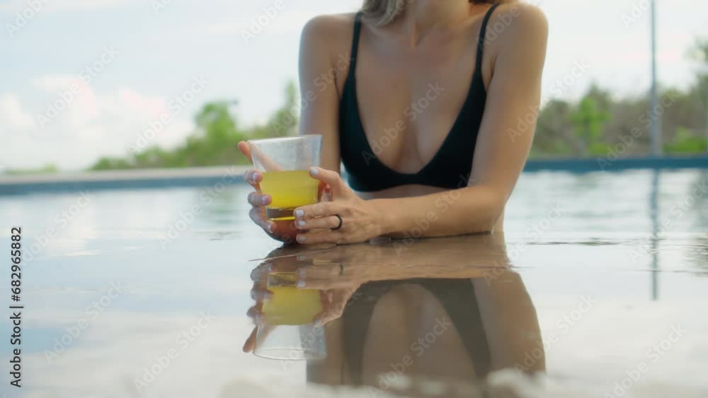 Girl sits in pool and picks up a glass of fresh orange juice Girl sits in pool and picks up a glass of fresh orange juice