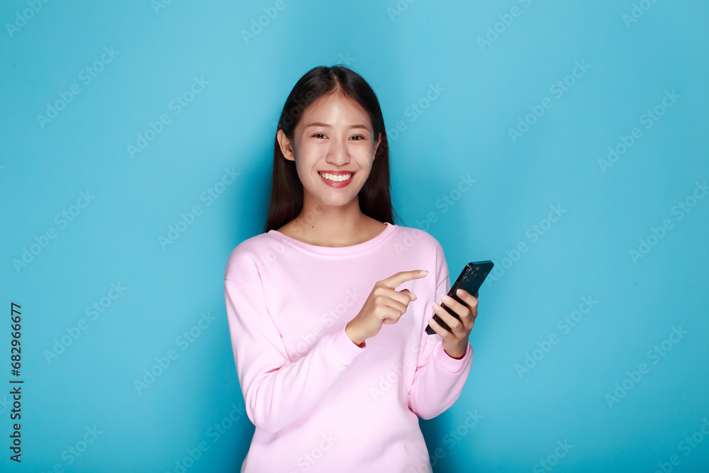Beautiful young woman in a light blue background, happy and smile, posting in stand position, A beautiful woman poses very cheerfully and happily while holding a cell phone in her other hand. Beautiful young woman in a light blue background, happy and smile, posting in stand position, A beautiful woman poses very cheerfully and happily while holding a cell phone in her other hand.