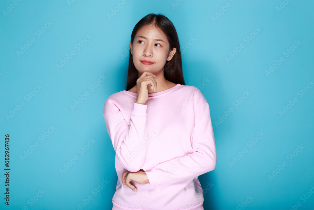Pretty girl makes a thoughtful expression, Portrait of a beautiful young woman in a light blue background, happy and smile, posting in stand position. Pretty girl makes a thoughtful expression, Portrait of a beautiful young woman in a light blue background, happy and smile, posting in stand position.