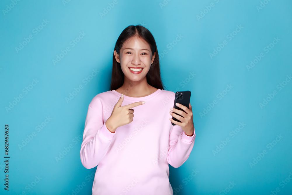 Beautiful young woman in a light blue background, happy and smile, posting in stand position, A beautiful woman poses very cheerfully and happily while holding a cell phone in her other hand. Beautiful young woman in a light blue background, happy and smile, posting in stand position, A beautiful woman poses very cheerfully and happily while holding a cell phone in her other hand.