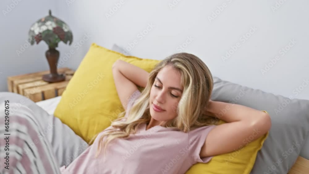 Blonde young woman lying relaxed in bed, indoors at home, resting her hands on her head, enjoying her comfortable bedroom, perfect for relaxation, complete morning wake up. Blonde young woman lying relaxed in bed, indoors at home, resting her hands on her head, enjoying her comfortable bedroom, perfect for relaxation, complete morning wake up.