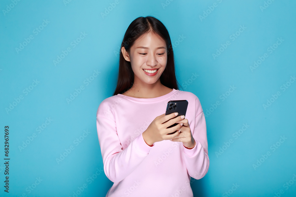 A woman has a blue background as a backdrop for a single portrait, smiling and holding a cell phone in her hand. A woman has a blue background as a backdrop for a single portrait, smiling and holding a cell phone in her hand.