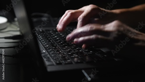 footage of a man's hands typing on a laptop keyboard 
dark lightning room in the frame, black colored laptop, light falls on hands photo
