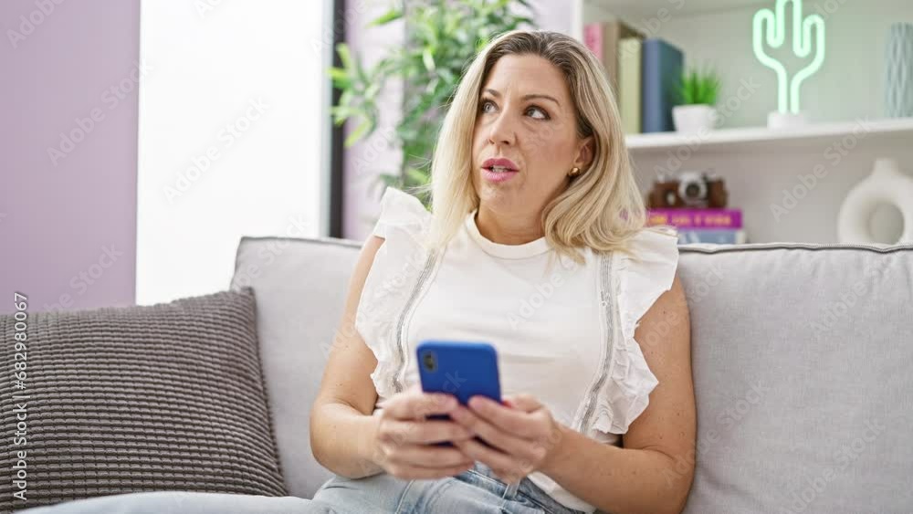 Young blonde woman using smartphone sitting on sofa thinking at home Young blonde woman using smartphone sitting on sofa thinking at home