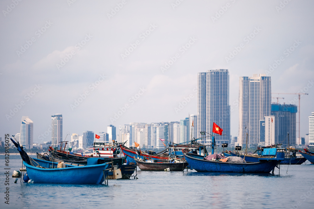 Selective focus on Vietnamese flag on fishing boat moored in port against coast with modern buildings. Da Nang cityscape in Vietnam..