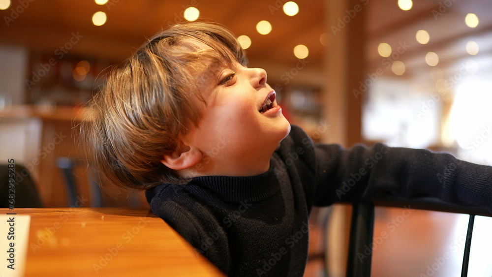 One small boy sitting at restaurant waiting for food to arrive feeling impatient and idle but with smile and happy One small boy sitting at restaurant waiting for food to arrive feeling impatient and idle but with smile and happy