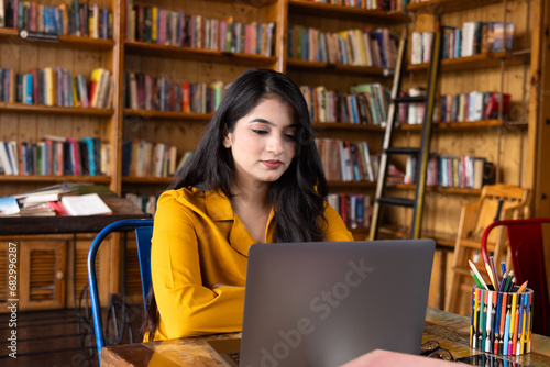 Beautiful young business woman girl student studying or explaining on video call on laptop in school or collage library or working in corporate office searching for information on internet or books
