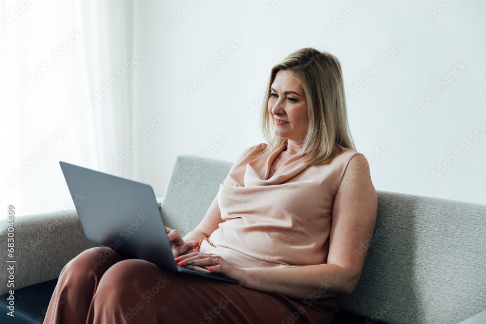 Naklejka premium Shot of a happy middle aged woman using her laptop on the sofa at home.